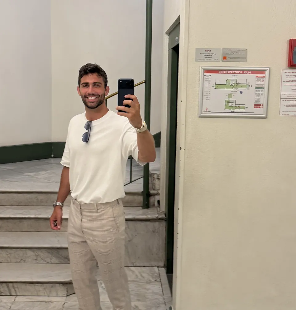 Thomas in a white tee and khakis taking a mirror selfie in a stairwell
